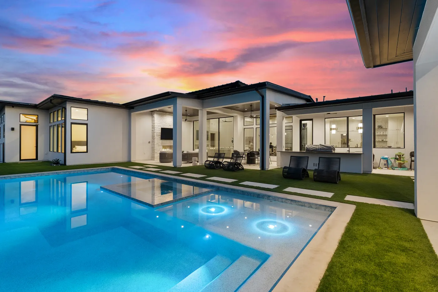 A lit pool and modern home under a pink dusk sky in the Hill Country
