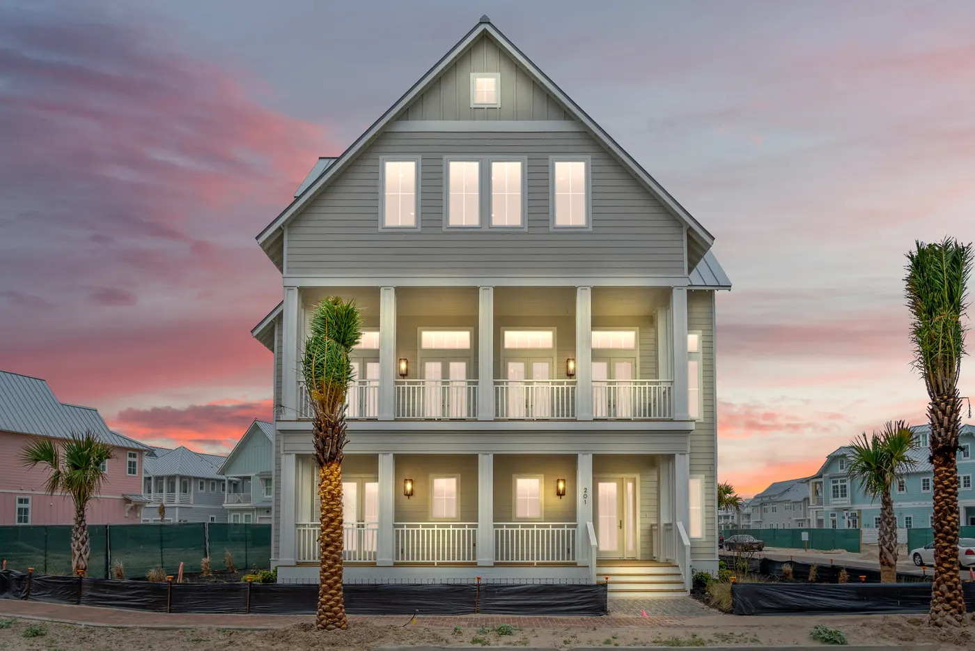A coastal home under a pink dusk sky, windows lit, palms at the drive