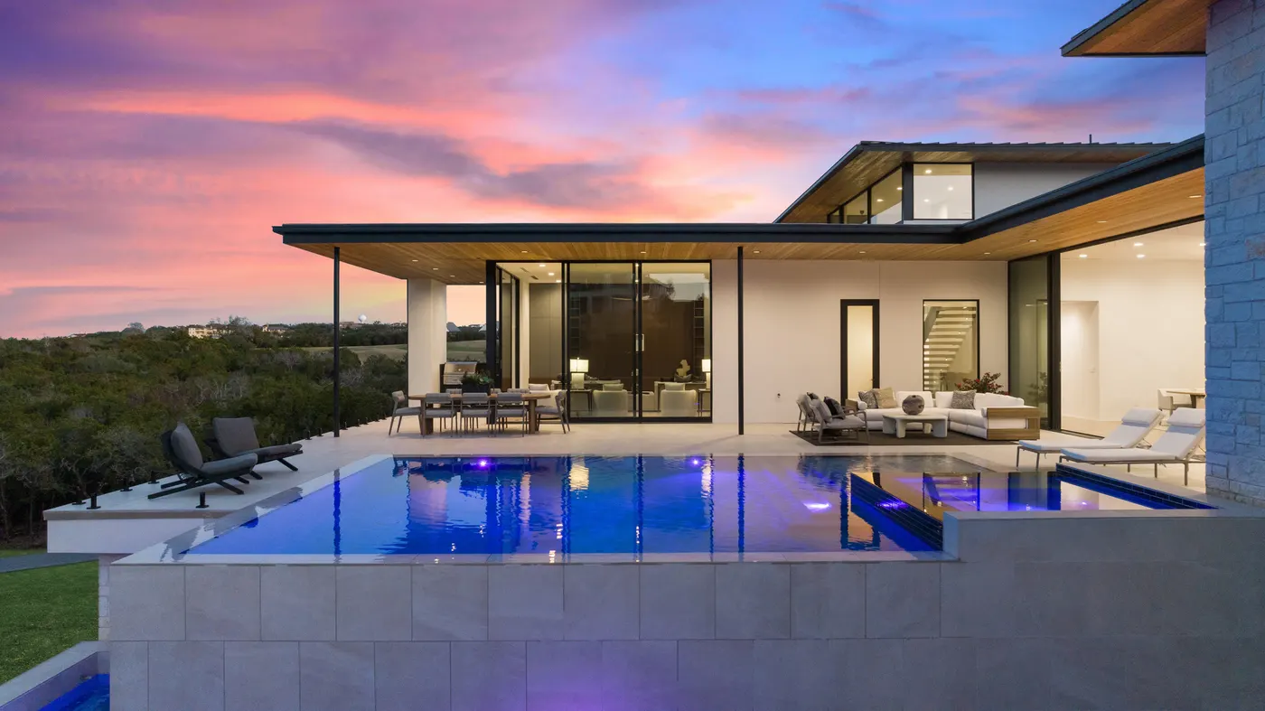 Infinity pool at sunset beside a modern glass-walled home